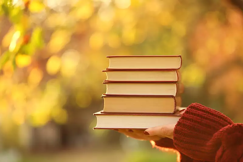 Pile of books in front of fall leaves