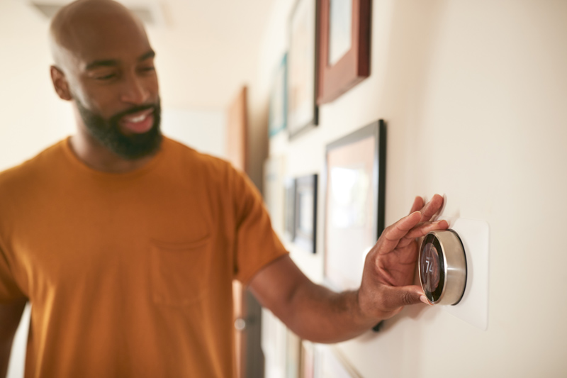 A homeowner turning on the air conditioner with the thermostat.