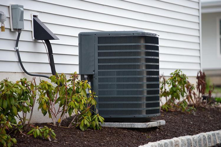 Air conditioner beside a home with green bushes.