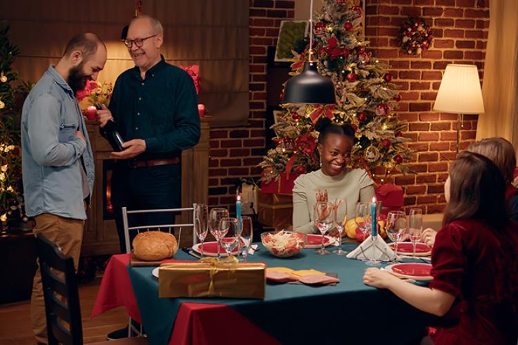 Group of people gathering for a meal around a table decorated for winter holidays.