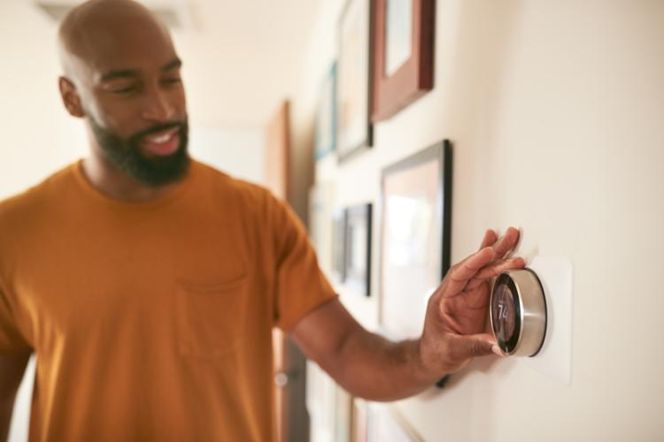 A homeowner turning on the air conditioner with the thermostat.